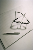 Sobre una hoja de papel, visto desde arriba, unas gafas y un bolígrafo.