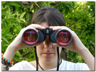 Mujer mirando de frente con unos enormes prismáticos. 