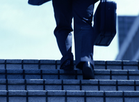 Piernas de un hombre subiendo unas escaleras con maletín en la mano derecha. 