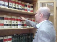 Imagen en la que se muestra a Carlos, situado enfrente de una estantería repleta de libros de leyes, y cogiendo uno de los libros con intención de consultarlo.