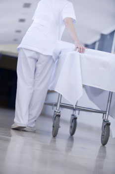 Una celadora de espaldas empuja una camilla de hospital 