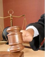 Imagen de un mazo de madera  que utilizan los jueces, siendo golpeado por la mano del juez, y detrás de él una balanza, símbolo de la justicia. 
