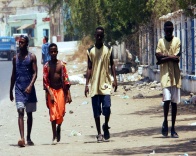 Cuatro hombres negros sin zapatos andando por una calle.