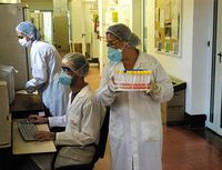 Trabajadores de laboratorio con bata y mascarilla realizando experimentos.