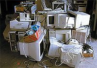 Varios monitores y equipos informáticos amontonados y un poco desordenados en el suelo de un almacén. 