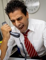 Un hombre en camisa y corbata, hace gestos un poco exagerados,  como de gritar,  a un teléfono que sujeta en la mano.