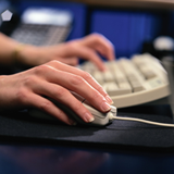 Primer plano de unas manos trabajando con un ordenador. La mano derecha sobre el ratón y la izquierda pulsa en el teclado. 