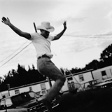 En blanco y negro, un hombre con sombrero baquero saltando en el aire.