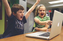 Un niño y una niña celebrando que algo funciona delante de la pantalla de un ordenador.