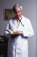 Un doctor, con pelo cano y bata blanca, sostiene en sus manos un libro. Al fondo una pared blanca con un título enmarcado.
