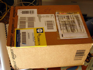 Imagen en la que se aprecia paquete postal, sobre la caja de cartón varias etiquetas de envío.