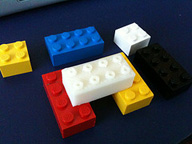 Piezas de lego de distintas formas y colores distribuidas encima de una superficie oscura.