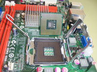 Muestra un zócalo del tipo LGA con las sujeciones abiertas  y un procesador preparado para su inserción.