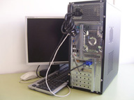 Vista posterior de la caja del ordenador  con el teclado, el ratón  y el monitor conectados. Se pueden apreciar los conectores de los tres periféricos.